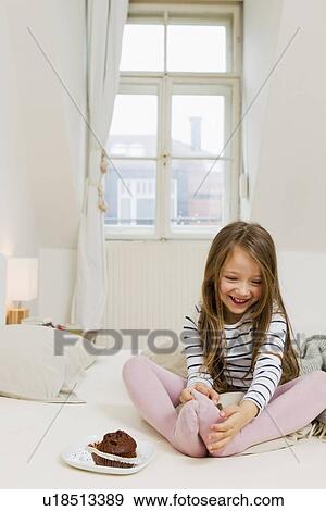 Stock Photo - Girl eating chocolate muffin on bed. Fotosearch