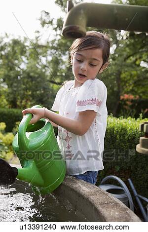 Stock Image - Girl filling up watering can in fountain. Fotosearch