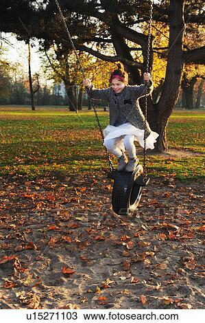 Stock Image - Girl playing on tire swing in park. Fotosearch