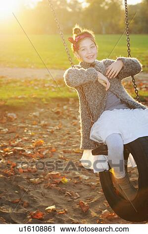 Stock Image - Girl playing on tire swing in park. Fotosearch