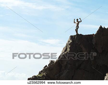 Picture - Man cheering on top of rocky hillside. Fotosearch