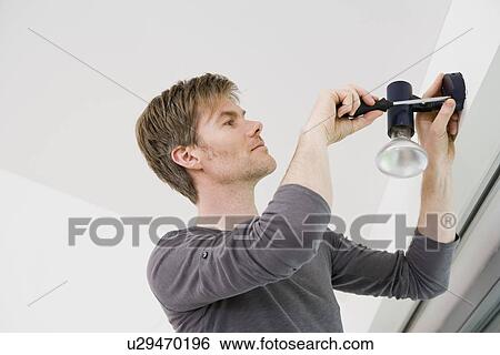 Stock Photograph - Man installing light fixture in house. Fotosearch