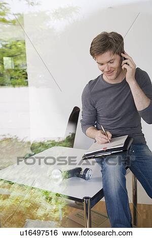 Stock Photograph - Man on cell phone taking notes. Fotosearch