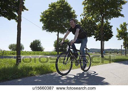 Man riding bicycle on rural road View Large Photo Image Stock Photo - Man riding bicycle on rural road. Fotosearch