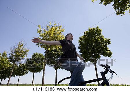 Stock Image - Man riding bicycle with no hands. Fotosearch