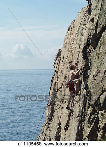 Man scaling coastal rock wall View Large Photo Image Stock Photo - Man scaling coastal rock wall. Fotosearch