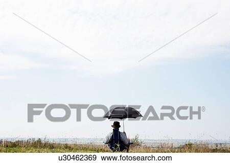 Man sitting under umbrella in field View Large Photo Image Stock Photo - Man sitting under umbrella in field. Fotosearch
