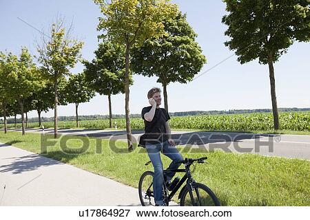 Man talking on cell phone on bicycle View Large Photo Image Stock Photo - Man talking on cell phone on bicycle. Fotosearch