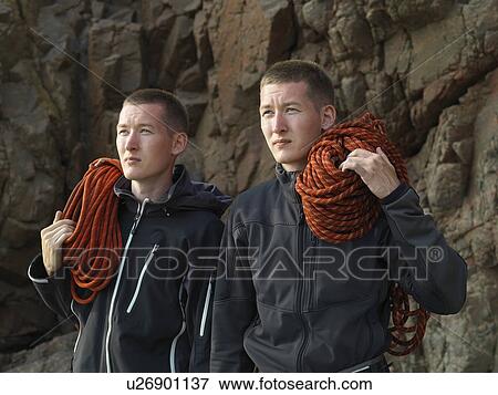 Stock Photo - Men carrying loops of rope on beach. Fotosearch