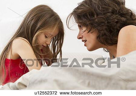 Stock Image - Mother and daughter talking on bed. Fotosearch