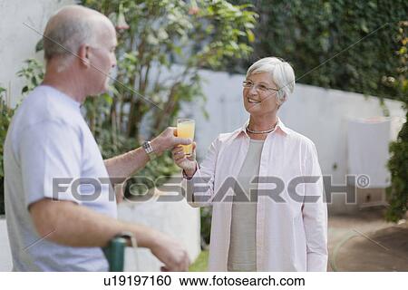 Stock Image - Older couple drinking juice in backyard. Fotosearch