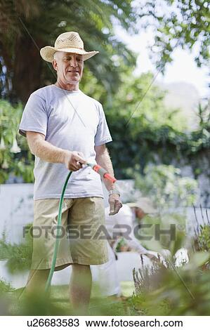 Stock Image - Older man watering plants in backyard. Fotosearch
