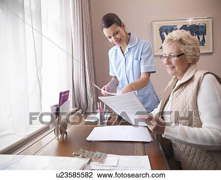 Stock Image - Older woman and nurse reading papers. Fotosearch