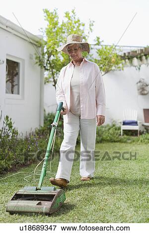 Stock Photo - Older woman mowing lawn in backyard. Fotosearch
