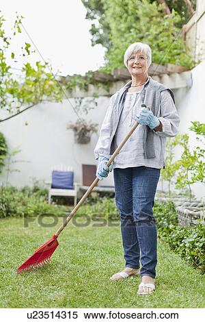 Stock Photography - Older woman raking in backyard. Fotosearch