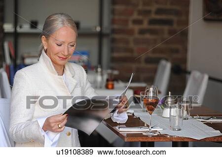 Stock Photo - Older woman reading magazine in cafe. Fotosearch