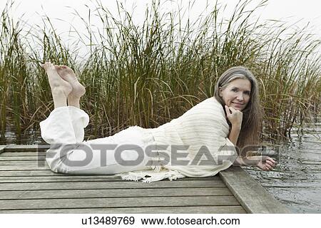 Stock Photo - Older woman relaxing on wooden dock. Fotosearch