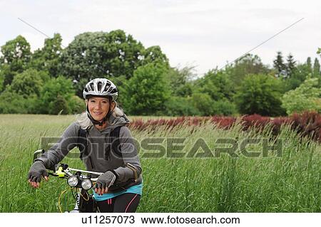Stock Image - Older woman riding bicycle on rural road. Fotosearch