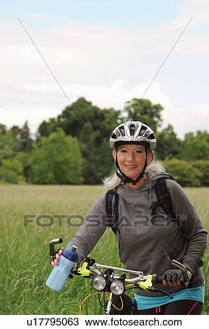 Stock Image - Older woman riding bicycle on rural road. Fotosearch