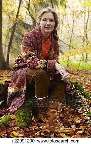 Stock Image - Older woman sitting on stump in forest. Fotosearch