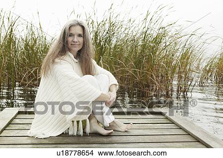 Older woman sitting on wooden dock View Large Photo Image Picture - Older woman sitting on wooden dock. Fotosearch