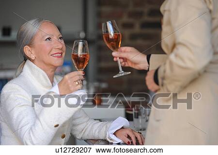 Stock Photo - Older women toasting each other in cafe. Fotosearch