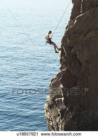 Stock Image - Rock climber rappelling down rock face. Fotosearch