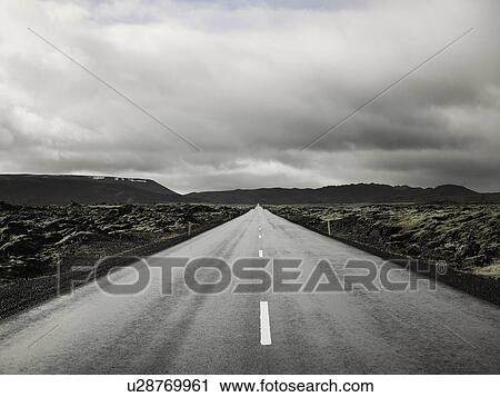 Stock Image - Rural road under cloudy sky. Fotosearch