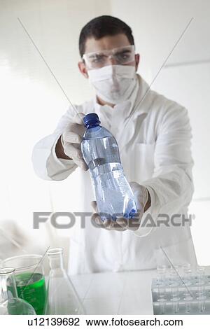 Stock Image - Scientist holding bottle of water in lab. Fotosearch