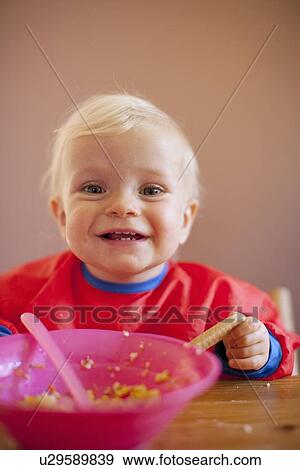 Smiling baby girl eating at table View Large Photo Image Stock Photo - Smiling baby girl eating at table. Fotosearch
