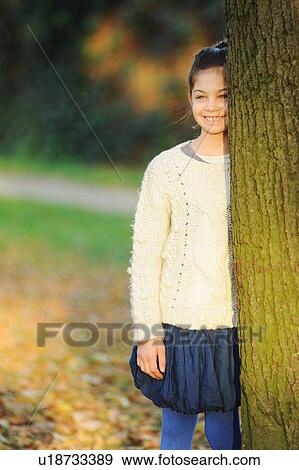 Stock Photo - Smiling girl leaning on tree in park. Fotosearch