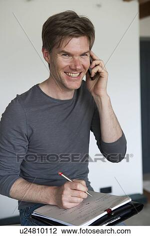 Stock Image - Smiling man on cell phone taking notes. Fotosearch
