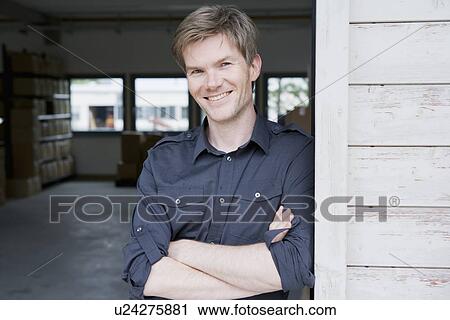 Stock Image - Smiling man standing in garage. Fotosearch