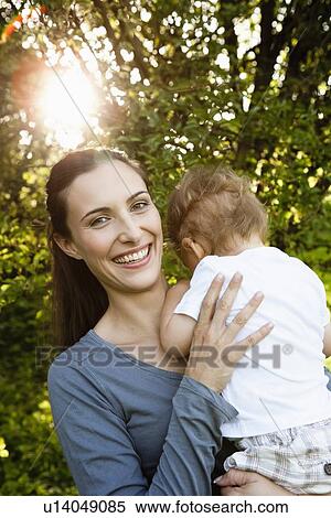 Stock Photography - Smiling mother holding toddler outdoors. Fotosearch