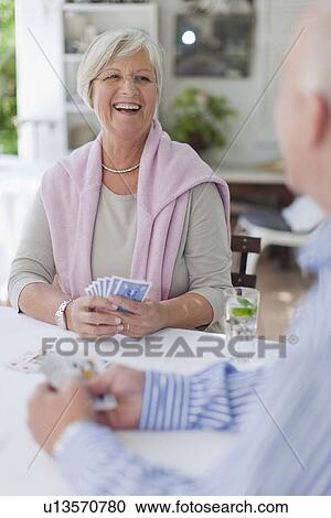 Stock Image - Smiling older couple playing cards. Fotosearch