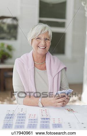 Stock Image - Smiling older woman playing cards. Fotosearch
