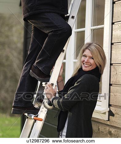 Stock Photograph - Smiling woman holding ladder for husband. Fotosearch