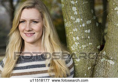 Stock Photo - Smiling woman leaning against tree. Fotosearch