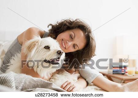 Stock Photo - Smiling woman petting dog in bed. Fotosearch