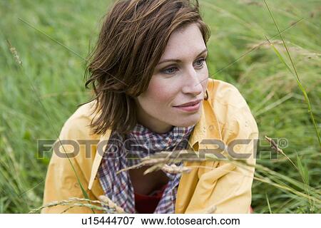 Stock Photo - Smiling woman sitting in tall grass. Fotosearch