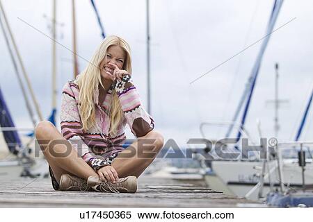 Stock Photography - Smiling woman sitting on wooden dock. Fotosearch