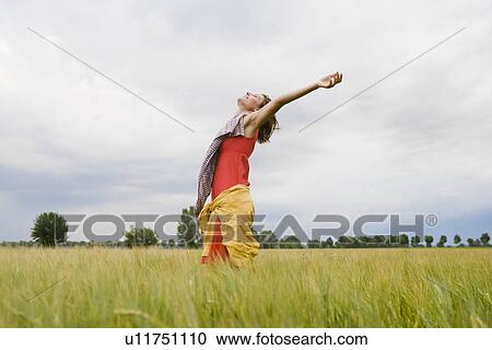 Stock Image - Smiling woman standing in tall grass. Fotosearch