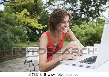 Smiling woman using laptop in backyard View Large Photo Image Stock Photograph - Smiling woman using laptop in backyard. Fotosearch