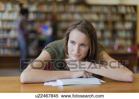 Stock Photography - Student resting chin on books in library. Fotosearch