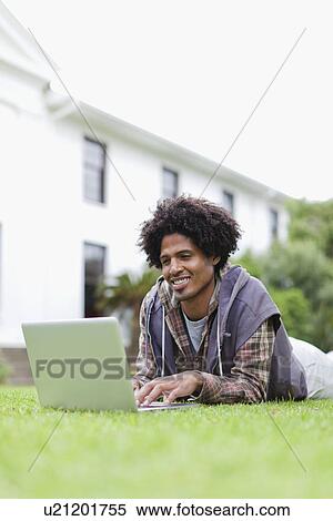 Stock Photography - Student using laptop on grass on campus. Fotosearch
