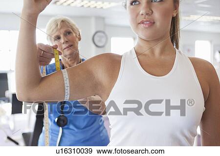 Stock Photo - Trainer measuring girls arm in gym. Fotosearch