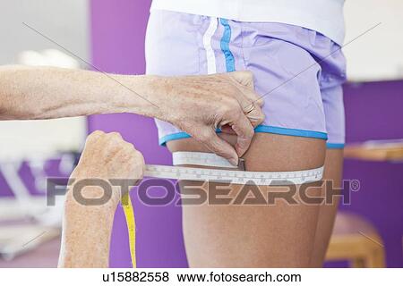 Stock Photo - Trainer measuring girls leg in gym. Fotosearch