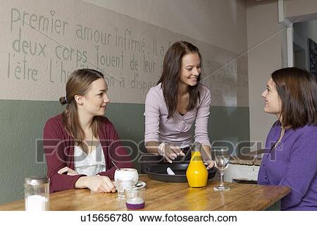 Stock Image - Waitress serving women in cafe. Fotosearch