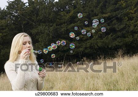 Stock Image - Woman blowing bubbles in wheatfield . Fotosearch
