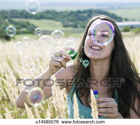 Stock Photograph - Woman blowing bubbles in wheatfield. Fotosearch